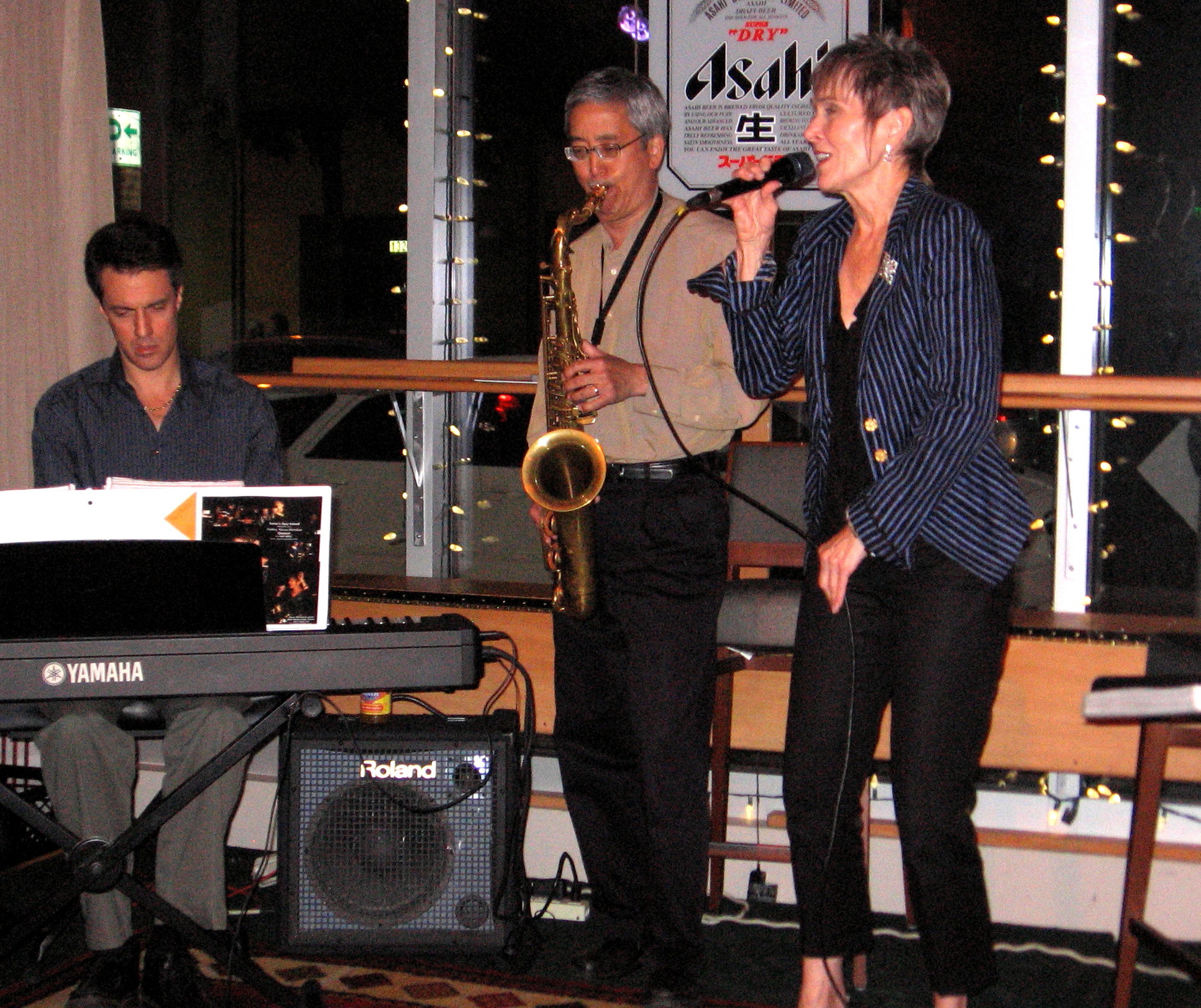 Audrey singing with pianist and saxophonist at a club window at night