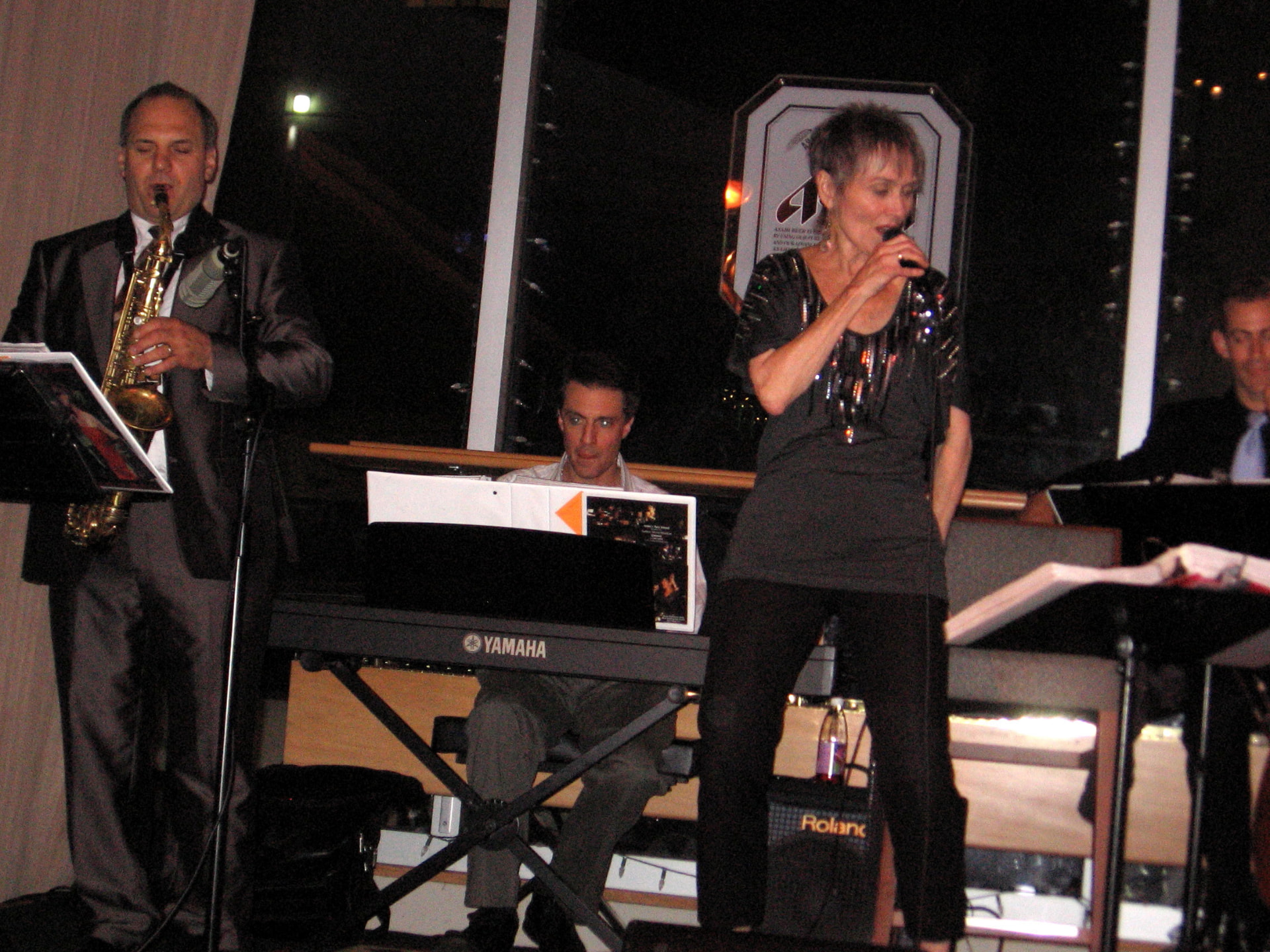 Audrey singing with saxophonist and pianist at an evening gala