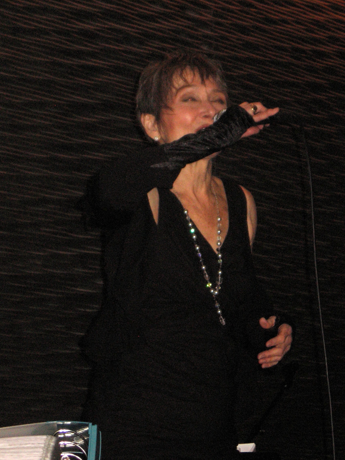 Audrey in black singing with her arm raised under stage light