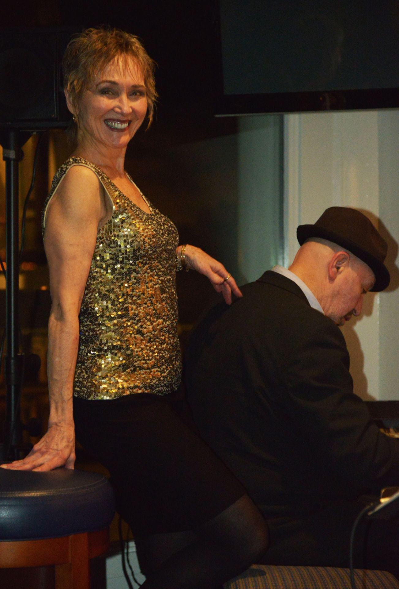 Audrey in a gold sequin top beside the pianist during a club set