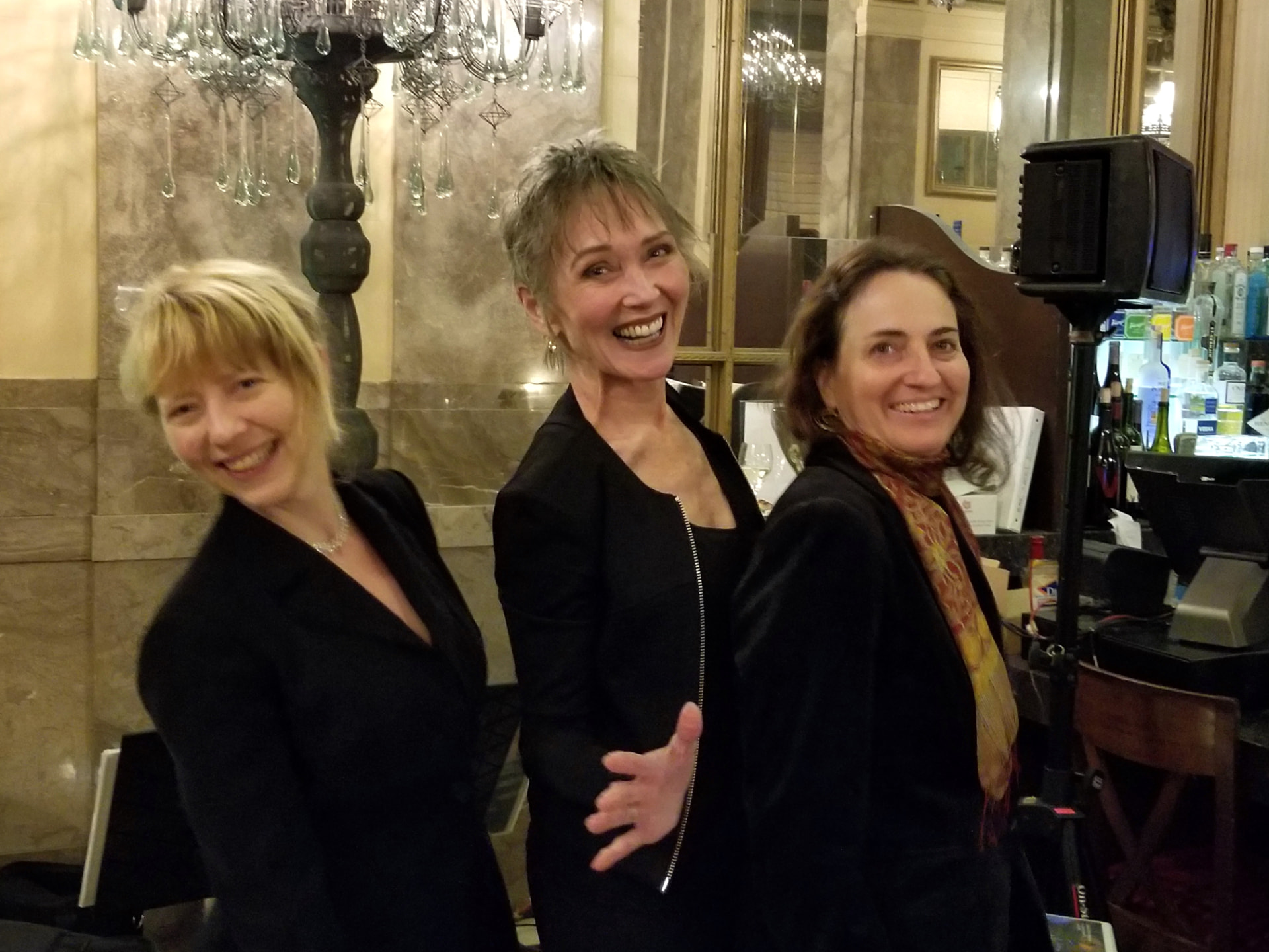 Audrey laughing with two bandmates beside a chandelier