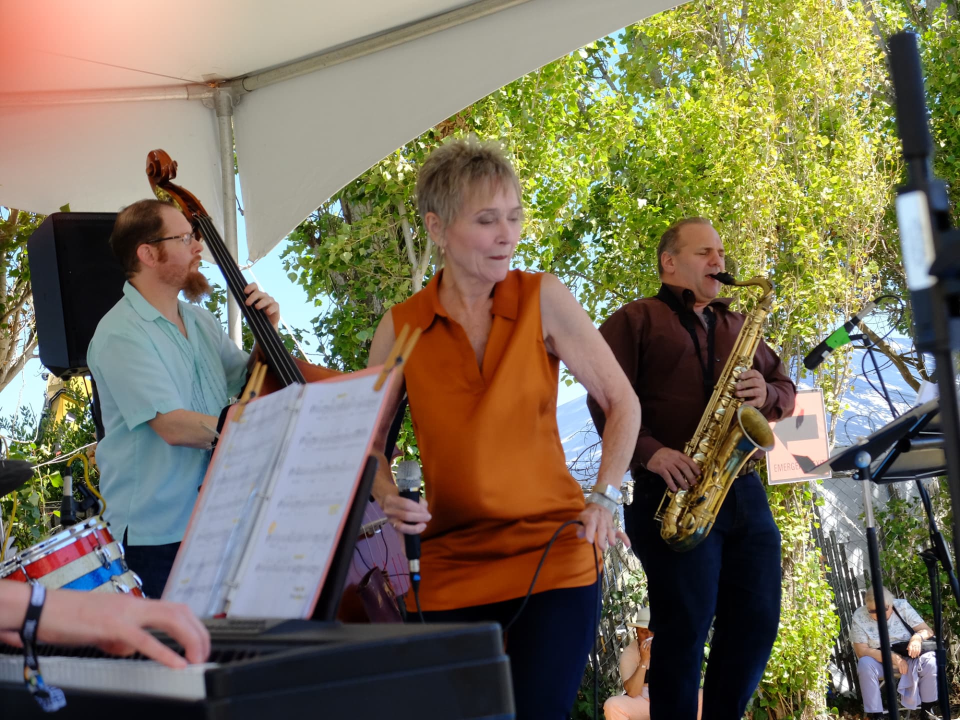 Audrey singing in an orange top with upright bass and saxophone at an outdoor festival